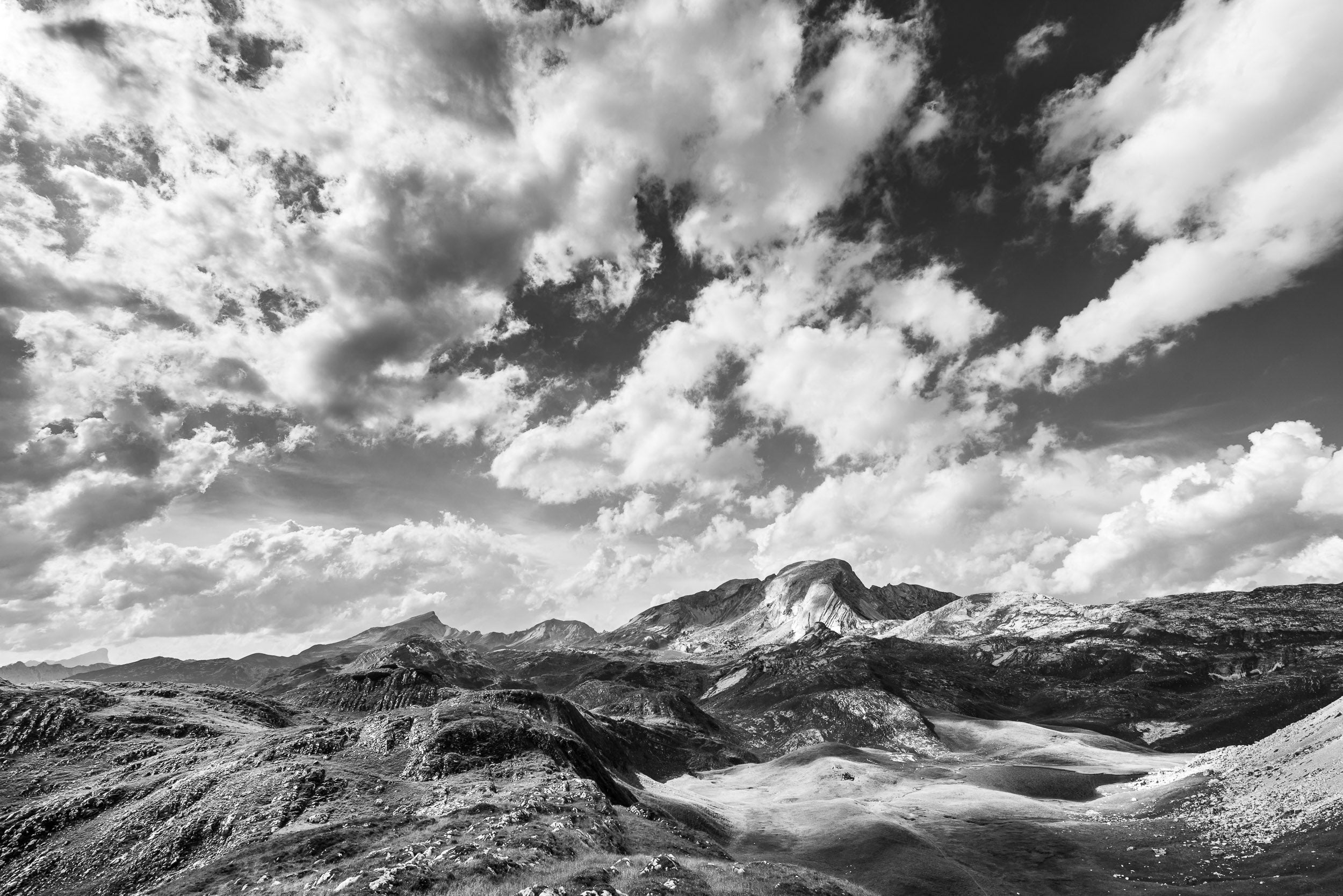 Fotografia in bianco e nero dell'Alpe di Foses con lago e Croda del Becco sovrastati da un cielo pieno di nuvole bianche
