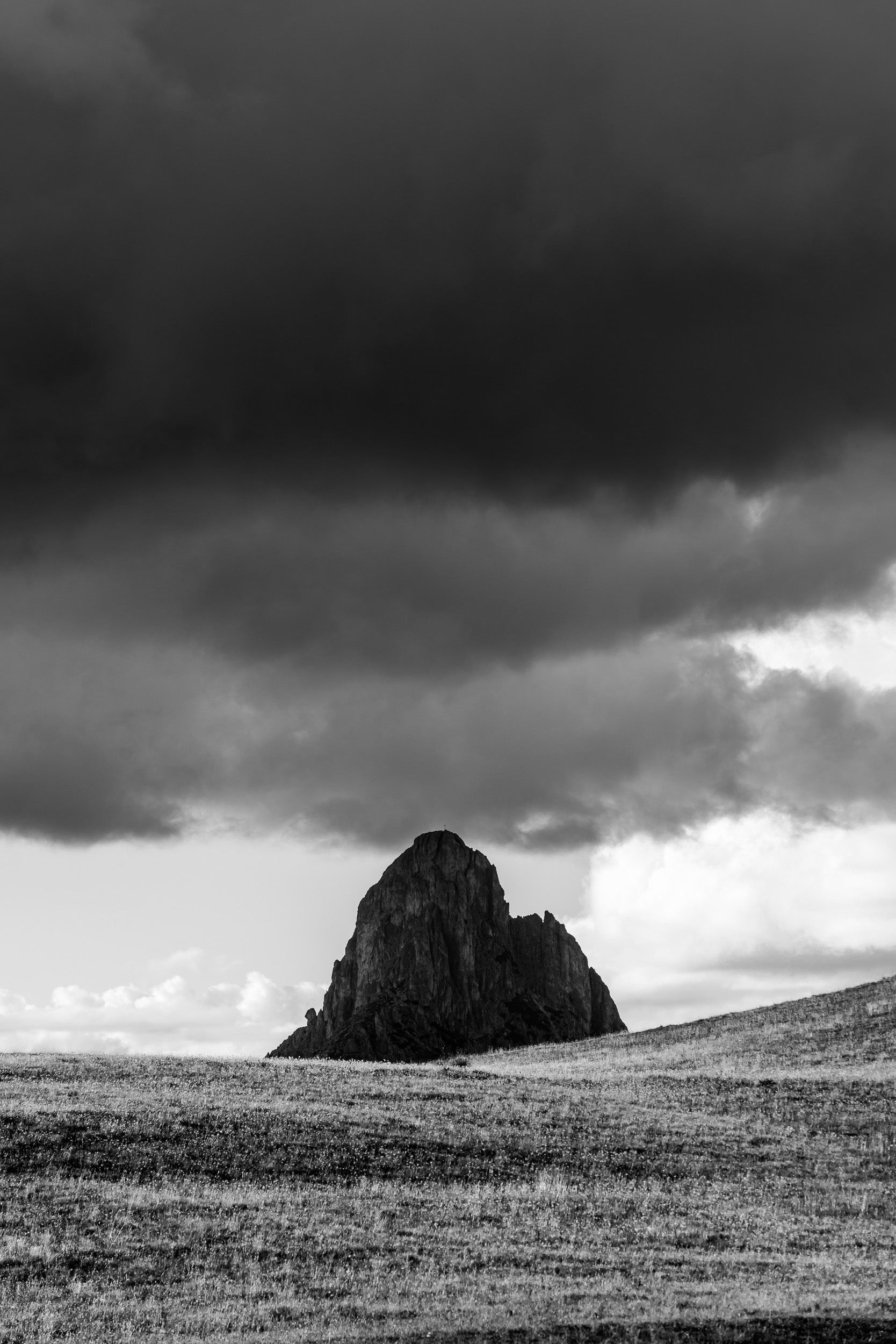 Fotografia verticale in bianco e nero del Sass de Stria. Atmosfera drammatica con montagna in ombra e cielo con scure nuvole minacciose