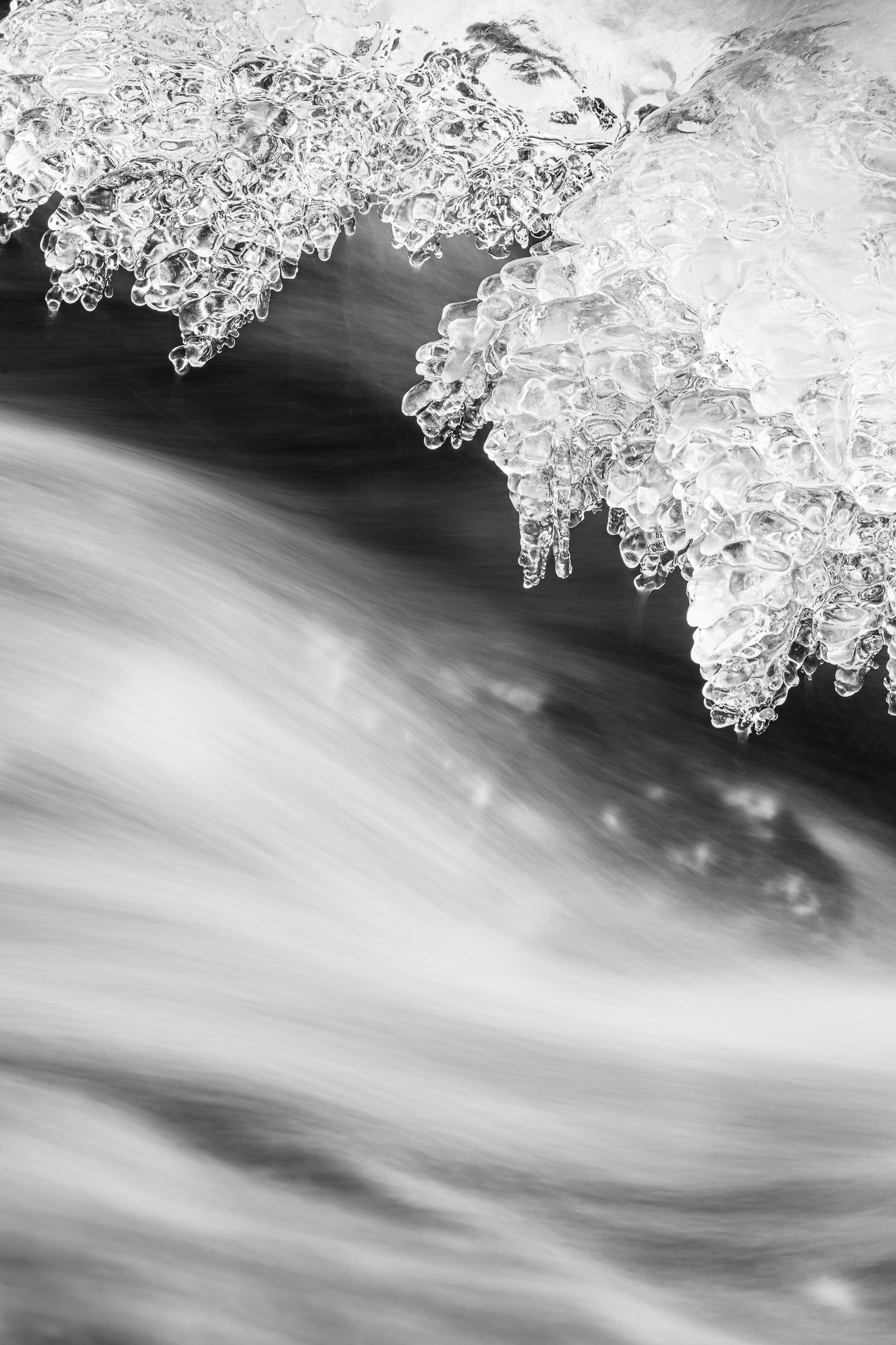 Fotografia verticale invernale in bianco e nero, con dettaglio su fiume con acqua in movimento e ghiacciata