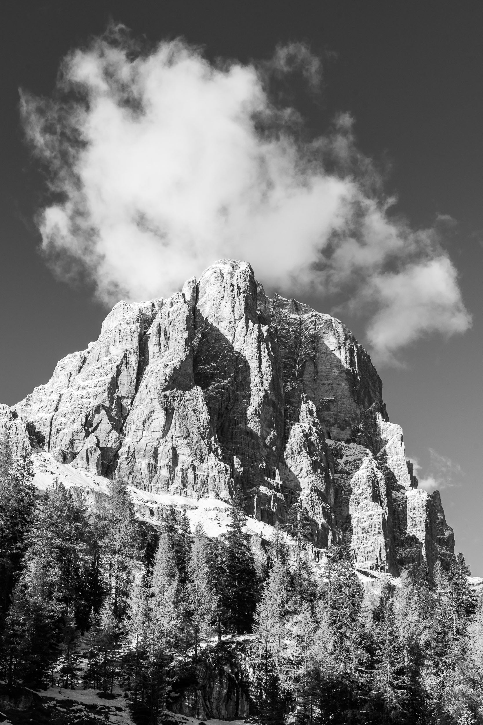 Fotografia verticale invernale in bianco e nero della Tofana di Rozes con neve autunnale e nuvola sulla cima