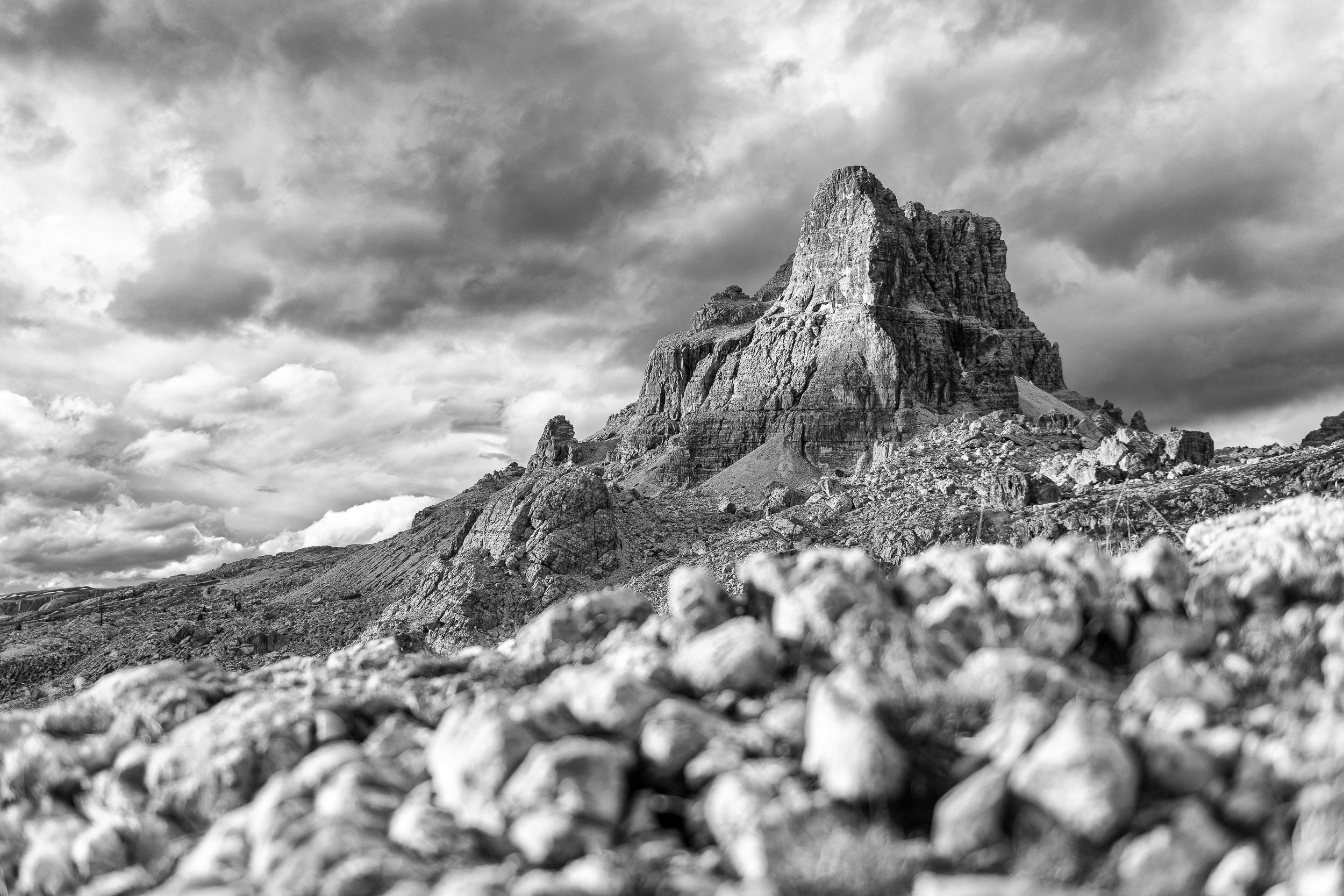 Fotografia in bianco e nero del Monte Averau con cielo nuvoloso. Le rocce in primo piano sfocate creano un senso di profondità.